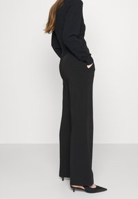 Czarne spodnie o szerokich nogawkach wykonane z gładkiego materiału, z ukośnymi bocznymi kieszeniami i wysokim stanem, w połączeniu z czarnymi szpilkami z wąskim noskiem.