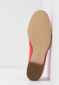 Chaussure plate en cuir rouge vue du côté de la semelle, avec semelle beige texturée et petit talon carré, marquée "högl" sur la semelle.