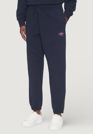 Pantalons de jogging bleu marine avec taille élastique et chevilles resserrées ; arbore un logo brodé rose sur la cuisse gauche ; fabriqué en tissu doux.