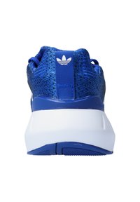 Zapatilla atlética azul con una parte superior texturizada, suela blanca y talón azul en contraste. Presenta un logo y un tirador en el talón para facilitar su uso.