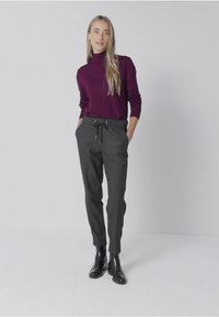 Burgundy polotröja och grå avslappnade byxor med dragsko. Modellen bär stiliga svarta ankellängds stövlar och står mot en ljus bakgrund.