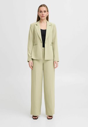 Svetle zelený přizpůsobený blazer a odpovídající kalhoty s širokými nohavicemi, vyrobené z hladkého materiálu, s jedním knoflíkem a bočními kapsami.