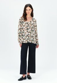 Blusa floreale nera, bianca, pesco e verde; vestibilità ampia, maniche lunghe, scollo a V, abbinata a jeans a gamba larga blu scuro e mocassini neri.