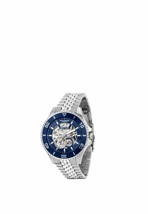 Orologio da polso in metallo argento con ghiera blu e ingranaggi interni visibili, con cinturino a maglie e quadrante tondo con marcatori numerati.