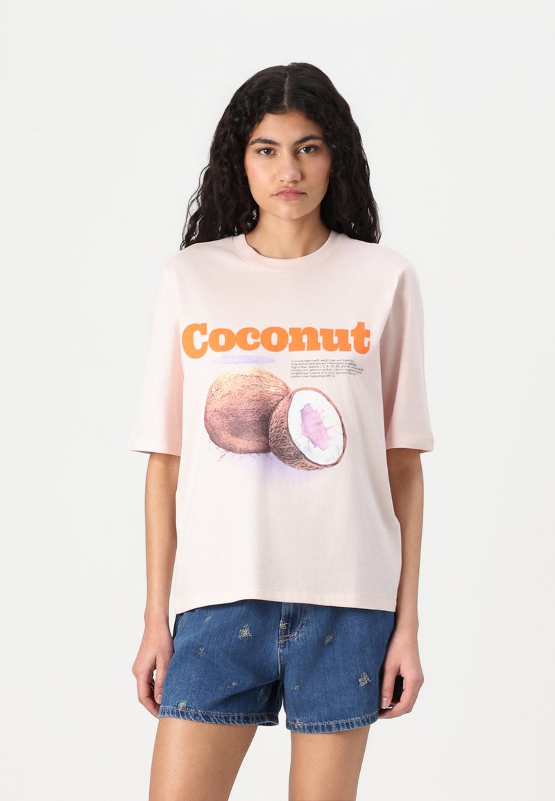 Lichtroze katoenen t-shirt met een afbeelding van een kokosnoot, voorzien van oranje tekst met de tekst "Kokosnoot" en gedetailleerde illustraties van de vrucht.