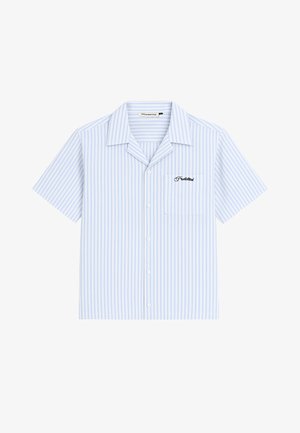 Frau trägt ein hellblaues, kurzärmeliges, gestreiftes Hemd mit Knöpfen und eine beige Baseballmütze mit Logo, steht vor einem einfarbigen Hintergrund.