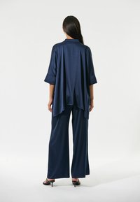 Ein samtiges, navyblaues Outfit mit einem lockeren Oberteil mit weiten Ärmeln und weit geschnittenen Hosen, die beide mühelos fallen. Schwarze High Heels vervollständigen den Look.