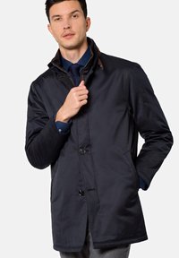 Granatowy płaszcz o gładkiej fakturze, zapinany na guziki, z brązowym kołnierzem. Posiada boczne kieszenie i prosty krój.