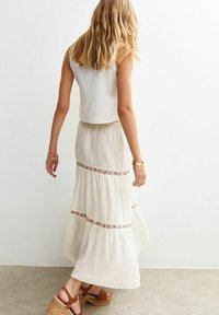 Un haut court blanc associé à une longue jupe à volants ornée d'une broderie florale et d'un motif texturé ; des sandales compensées en liège marron.