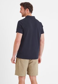 Navy polo shirt with short sleeves, fitted design, and visible collar; paired with beige knee-length shorts and textured fabric details.