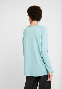 Light blue long-sleeve shirt with a relaxed fit, featuring a crew neck and slight texture. The hem is curved, showing minimal stitching.