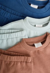 Kolm rõivaeset: tumel sinine ümarkaelusega pusa, heleroheline ümarkaelusega pusa ja pruun ümarkaelusega pusa, kõigil soonikkoelised kraed ja pehmed tekstuurid.