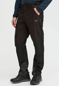 Schwarze Outdoor-Hosen aus robustem Material, mit einer Reißverschlusstasche, einem Design mit mehreren Taschen und verstärkten unteren Bereichen für zusätzliche Stärke.