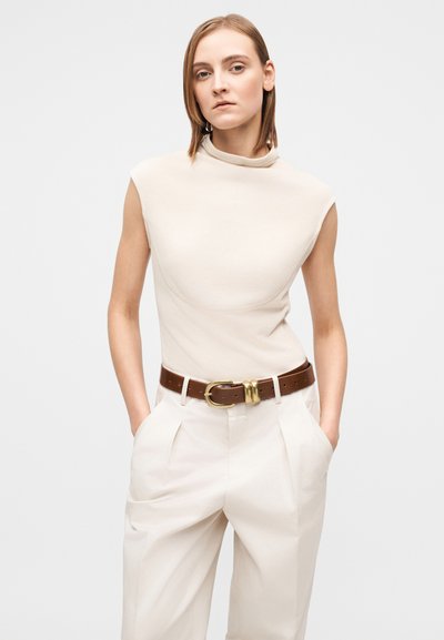 Beigeä istuva yläosa korkealla kauluksella, yhdistetty vaaleabeigeihin housuihin ja ruskeaan vyöhön, jossa on kultainen solki, sileä kangaspinta.