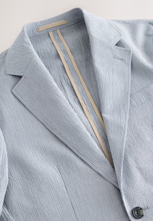 Hele sinine ja valge triibuline bleiser, valmistatud kergelt tekstuurse kangaga, millel on mitte-märgistuskaelus, ühe nupuga kinnis ja beež vooder.