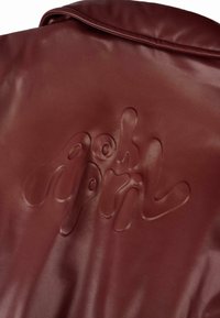 Giacca in pelle bordeaux con logo del marchio in rilievo, finitura lucida e texture liscia. Il design include un colletto piegato e linee pulite.