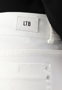 Un jean en denim blanc avec une étiquette en cuir portant le texte "LTB", des boutons en métal argenté et un tissu lisse et texturé à la taille.