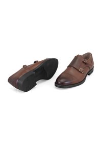 Bruine leren schoenen met dubbele gespbanden, ronde neus en decoratieve perforaties. Zwarte rubberen zool met profielpatroon.