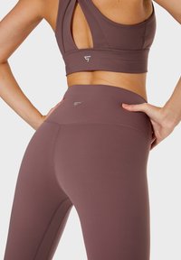 Set di reggiseno sportivo e leggings in un tenue color mauve. Il reggiseno ha un design a schiena scoperta con dettagli ritagliati; i leggings presentano una vita alta e un logo discreto.