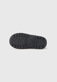 Black rubber shoe sole with a textured tread pattern, featuring deep grooves and raised sections for grip and durability.
