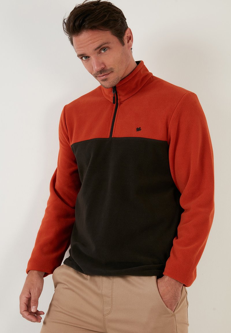 Fleece pullover with a half-zip design; features orange upper and black lower sections, soft texture, and a small logo on the chest.