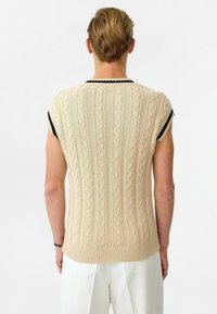 Gebreid kortemouwen trui in beige met kabelpatroon, voorzien van een zwarte ribbelsboord. Textuur is soepel met een aansluitend ontwerp.