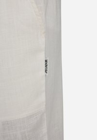White linen fabric with a soft texture, featuring a side pocket and a visible brand tag labeled "PEGADOR."