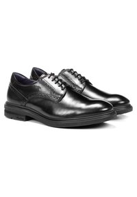 Chaussures de ville en cuir noir avec des orteils arrondis, accents de brogue détaillés et semelle en caoutchouc noir texturé contrastante. Design classique à lacets.