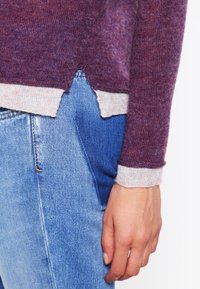 Sweter dzianinowy w gradientowych odcieniach fioletu z jasnoszarym mankietem i krawędzią, zestawiony z niebieskimi dżinsami z przednią kieszenią.