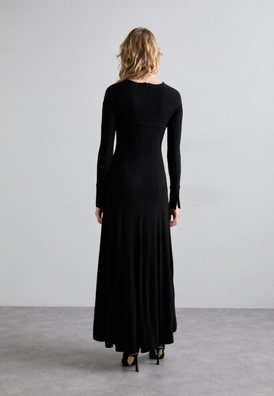 Vestido negro de manga larga con un corsé ajustado y falda acampanada, hecho de material elástico. Cuenta con un cierre en la parte posterior y puños con abertura.