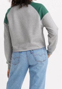 Sweat-shirt gris avec manches raglan vertes, coupe courte, texture douce, associé à un jean bleu clair taille haute avec poches arrière.