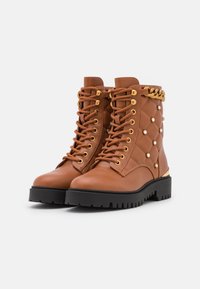 Bottes en cuir marron avec un design matelassé, ferrures dorées, lacets et accents décoratifs en perles. Semelle en caoutchouc noire pour plus d'adhérence.