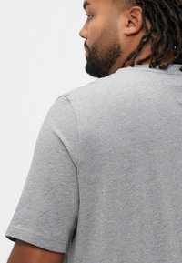 Szary T-shirt z krótkim rękawem wykonany z miękkiej, teksturowanej tkaniny, z klasycznym okrągłym dekoltem i luźnym krojem. Widok z tyłu ukazuje detale szwa na ramionach.