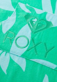 Turquoise strandlaken met witte bladerenpatronen, textuur oppervlakte en een reliëf "ROXY" logo met een hartontwerp.