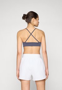 Grå sport-bh med korsade remmar, parat med vita shorts med elastisk midja. Slät tyg, enkel design och minimal detaljering.