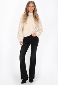 Beżowy sweter z teksturowanymi, koronczastymi rękawami z ozdobami, w połączeniu z czarnymi dzwonami i czarnymi botkami za kostkę.