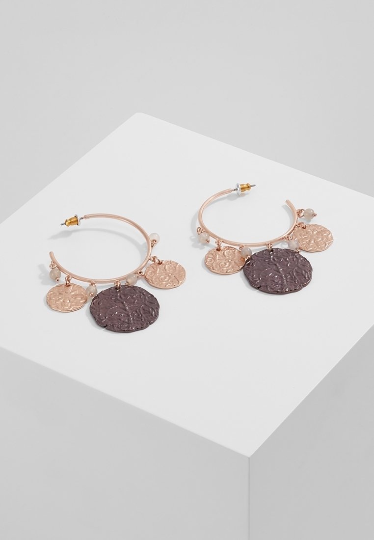 Boucles d'oreilles créoles en or rose avec des breloques rondes texturées en or rose et métal sombre, exposées sur un socle blanc.