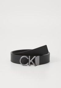 Schwarzer Leder Gürtel mit einem eleganten Design, ausgestattet mit einer runden silbernen Schnalle mit den Initialen "CK" und einer durchgehend glatten Oberfläche.