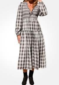 Schwarz-weiß kariertes Kleid mit gerafftem Oberteil, langen Puffärmel und gestuftem Rock. Verfügt über einen V-Ausschnitt und eine Bindung hinten.