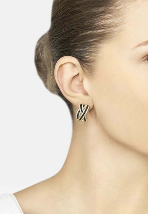 Gold-tone earring with black and clear rhinestones in a twisted ribbon design worn on a woman's left ear with hair pulled back.