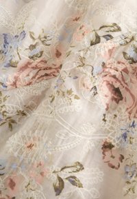 Doorzichtige stof met een zacht pastelbloemenprint en witte geborduurde blad- en bloemmotieven op een lichte achtergrond.