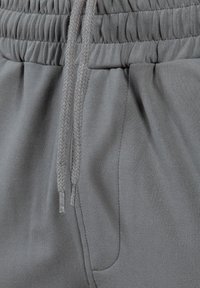 Grå joggerbukser med elastisk talje og justerbare snore, sidelommer og en glat tekstur.