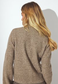 Pull en tricot marron avec un ourlet côtelé, un col en V et une coupe décontractée. Le tissu semble doux avec une surface légèrement texturée.