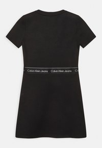 Černé šaty s krátkým rukávem z bavlněné směsi, s přiléhavým korzetem a rozšířenou sukní, s bílým páskem značky s nápisem "Calvin Klein Jeans."