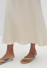Light beige, flowing midi dress with a scalloped hem and subtle side seams; paired with light tan flip-flops featuring a low heel.