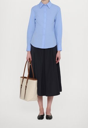 Chemise moulante bleu clair à boutons, jupe midi noire, ballerines noires, et sac fourre-tout beige avec des anses et des accents marron.