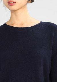 Maglione blu navy con scollatura ampia, texture a costine e vestibilità morbida. Realizzato in tessuto morbido, con maniche lunghe e dettagli minimi.