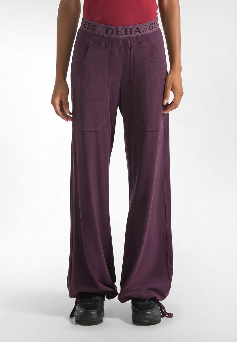 Paarse relaxte broek met een wijde pijpdesign, gemaakt van zacht materiaal; heeft een zwarte elastische tailleband met merknaam en zijzakken.