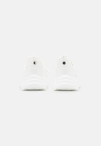 Hvide atletiksko med en glat syntetisk overdel, åndbare mesh-detaljer og en polstret sål med teksturerede greb.