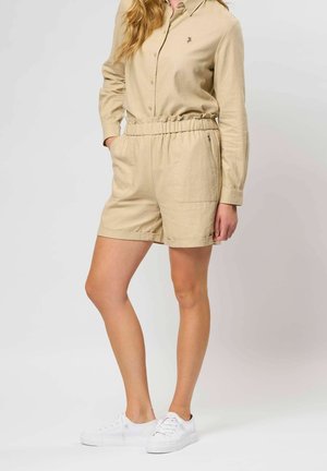 Cămașă bej din in cu guler, pantaloni scurți cu talie elastică, buzunare laterale și adidași albi. Detaliată cu un mic design brodat pe cămașă.